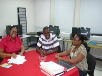 2 women and a man discuss matters seated at a table that has a stack of documents