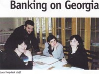 Picture from Newspaper article of a man standing with 3 women seated at a desk with documents