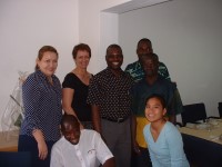 2 women and 3 men stand smiling behind a seated man and woman