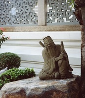 a pale stone statue of a warrior in contemplation sits on a boulder